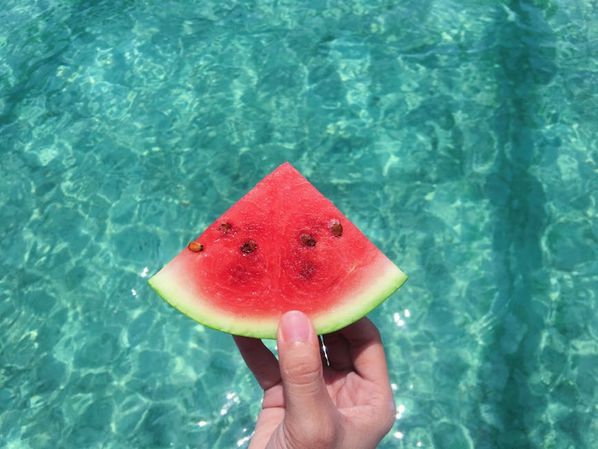 Hand holding a ripe watermelon slice with a turquoise pool background, perfect summer vibes.